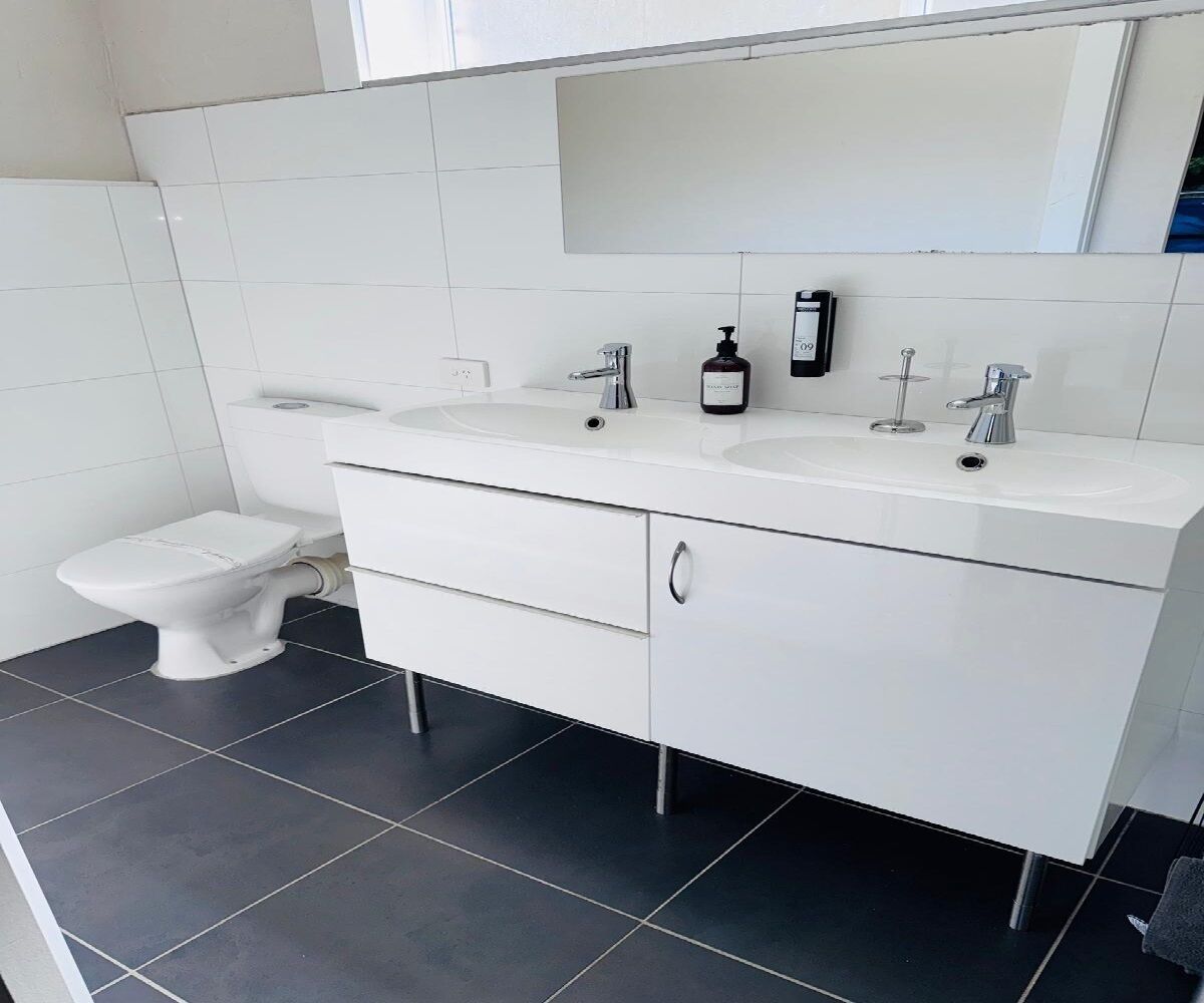 Un baño moderno con un tocador blanco, dos lavamanos, un inodoro y un espejo sobre el tocador.