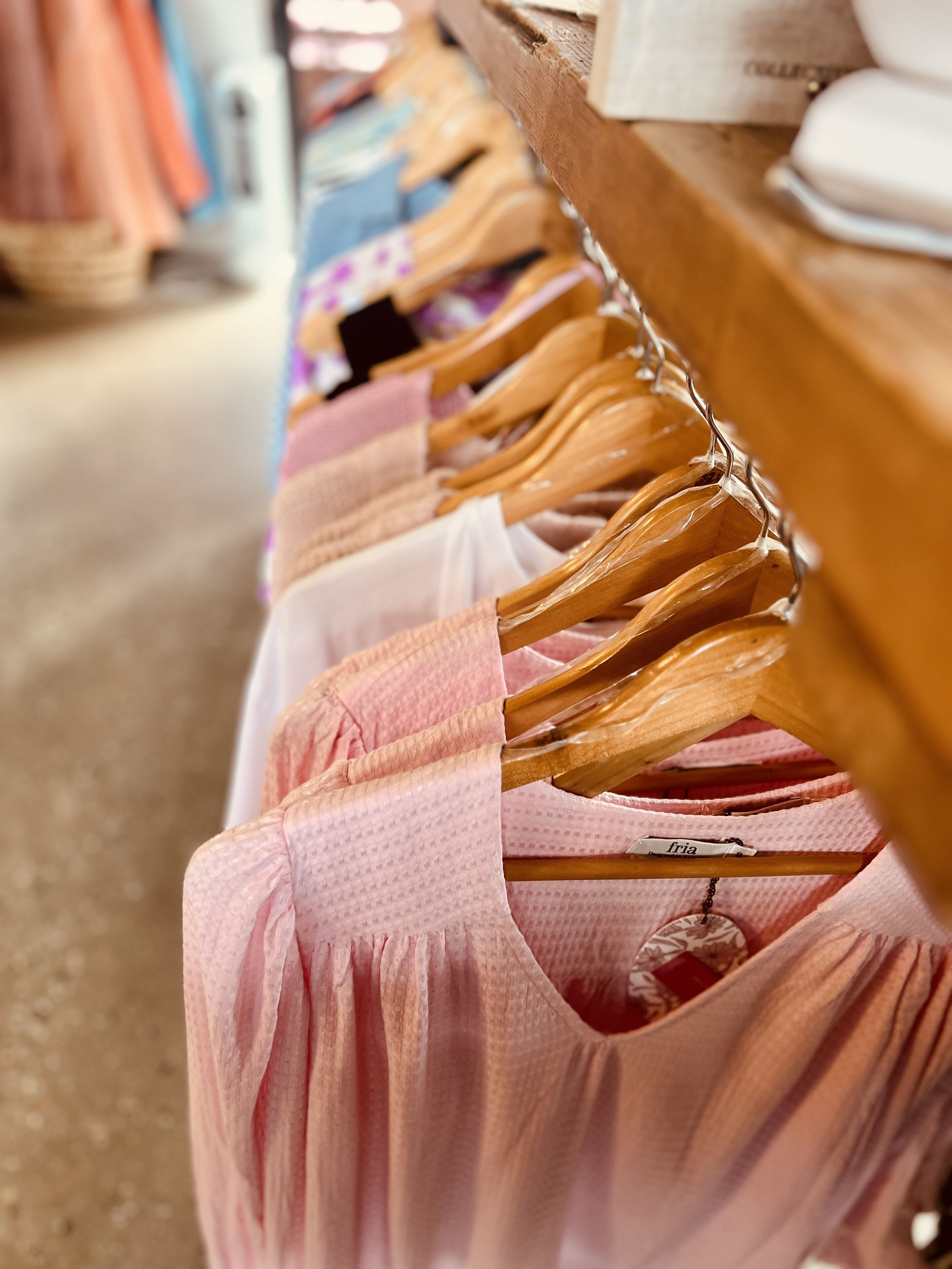 A clothing rack with various garments, including a pink dress with a name tag.