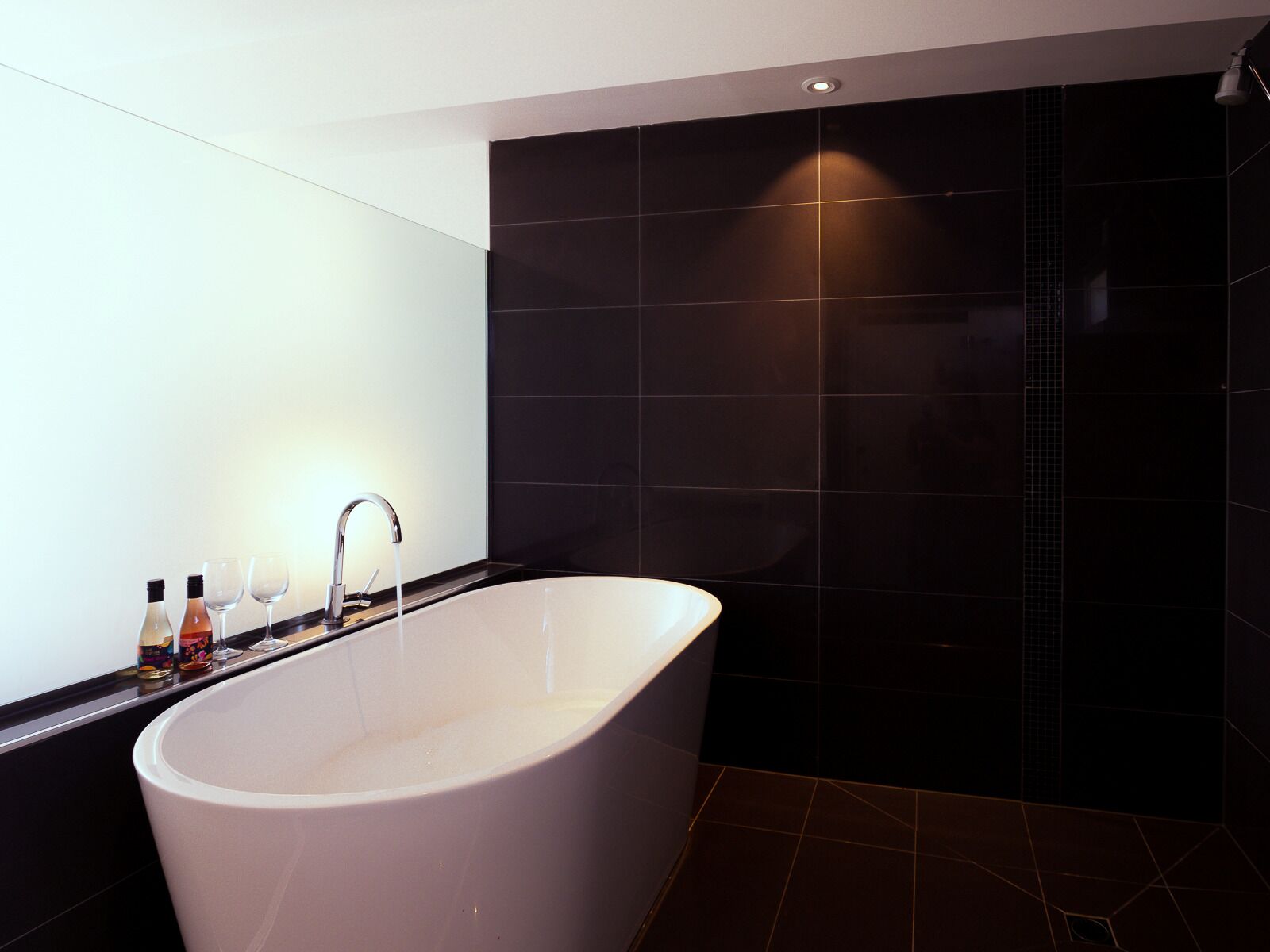 Un baño moderno con una bañera independiente, paredes de azulejos oscuros y un diseño minimalista.