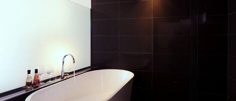 Un baño moderno con una bañera independiente, paredes de azulejos oscuros y un diseño minimalista.
