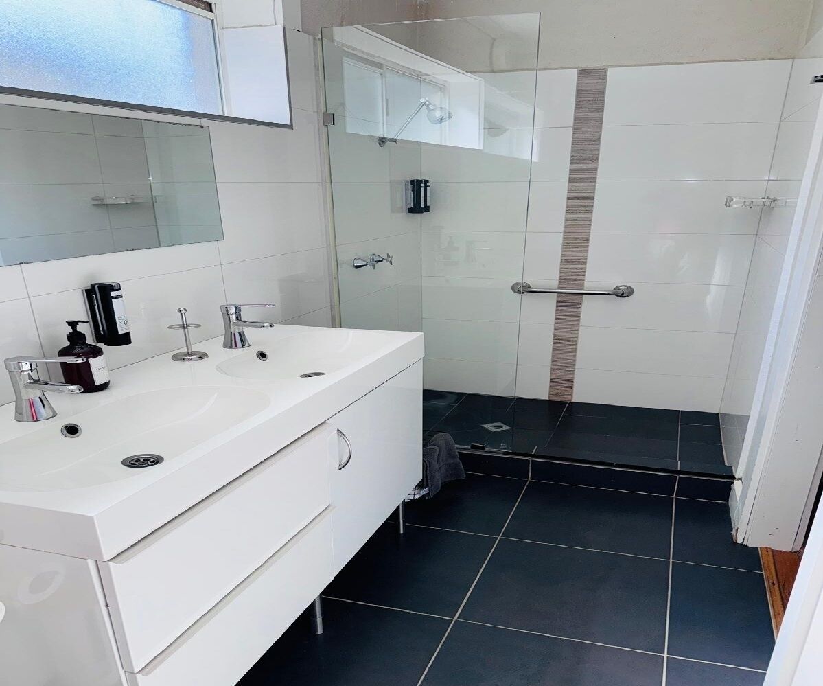 A modern bathroom with a white vanity, a glass shower enclosure, and black tiled flooring.
