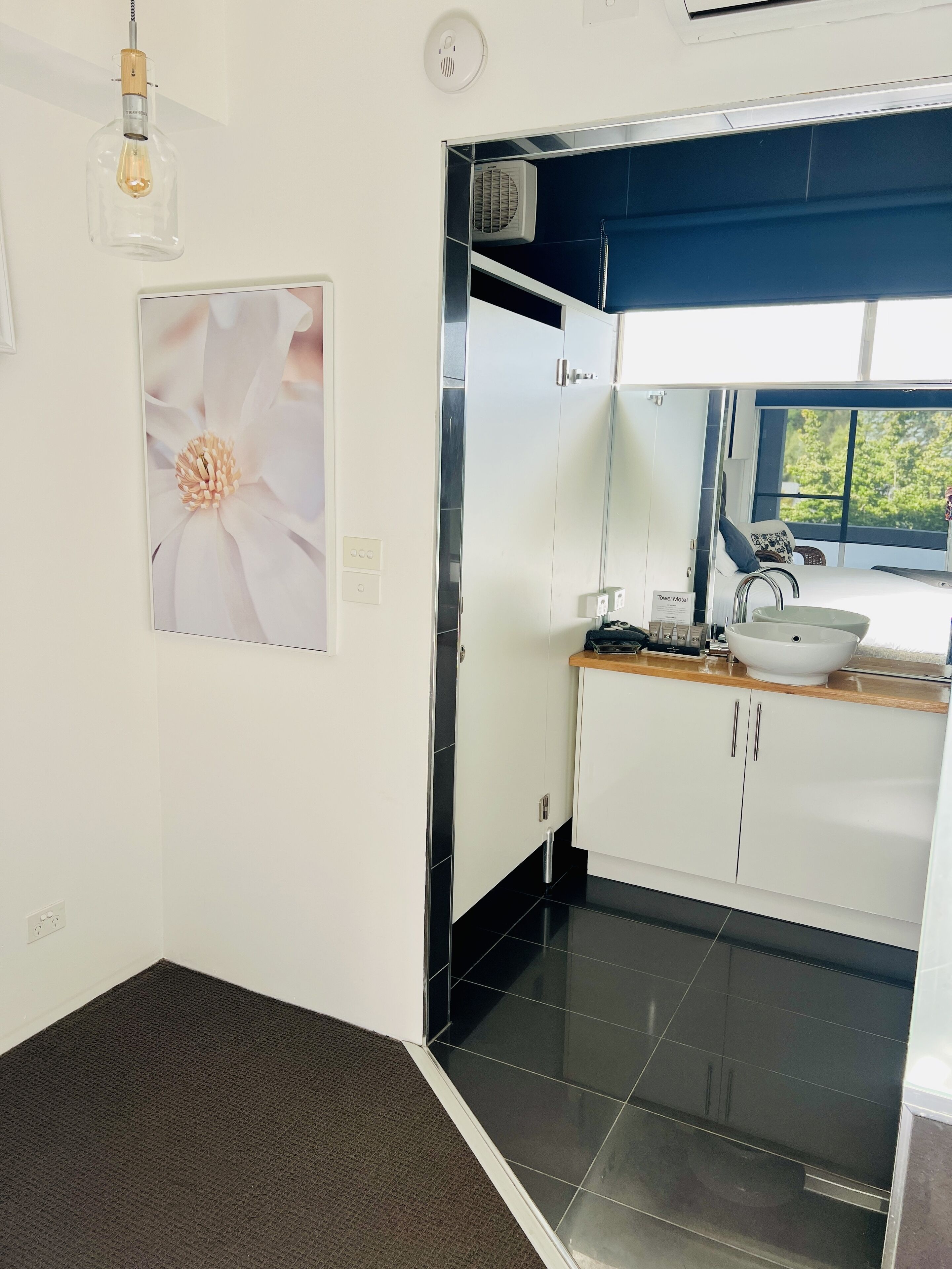 Un baño moderno con un lavabo blanco, un espejo y un inodoro. En la pared, un cuadro con una flor.