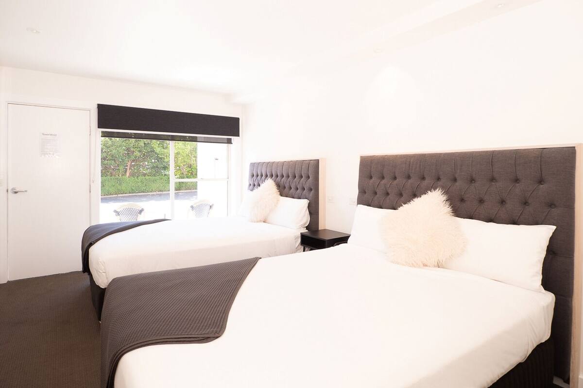 Una habitación de hotel con dos camas, un ventanal grande y una puerta.