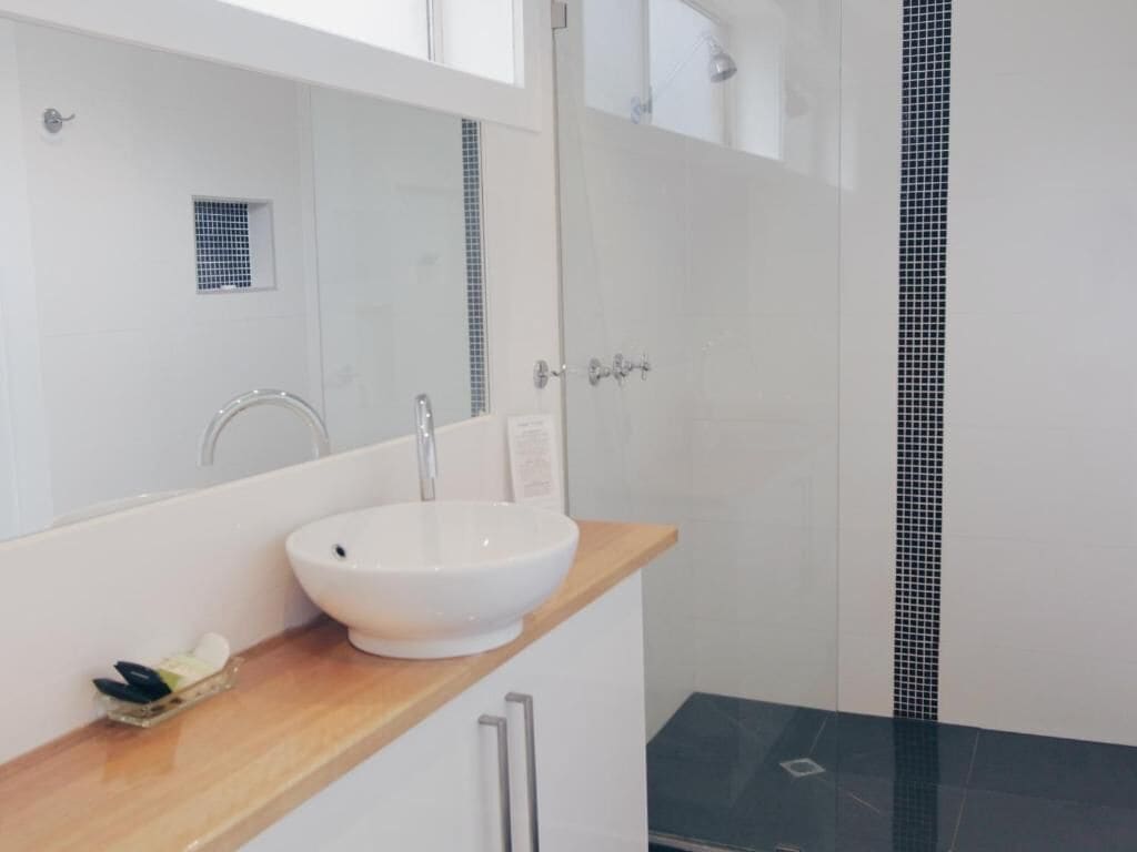 A bathroom with a white sink, a wooden countertop, and a mirror above it.
