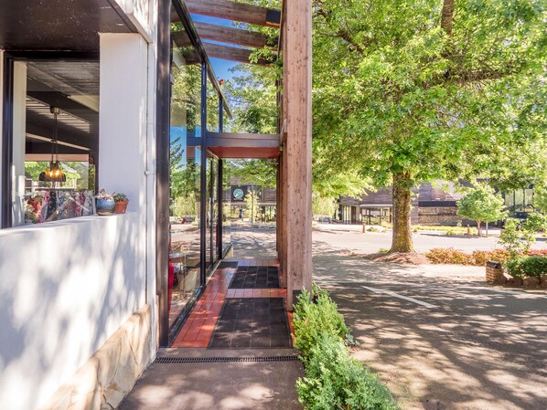 A covered outdoor area with a wooden pergola, a pathway leading to a building entrance, and a view of a parking lot and trees. - Tower Motel (Marysville)