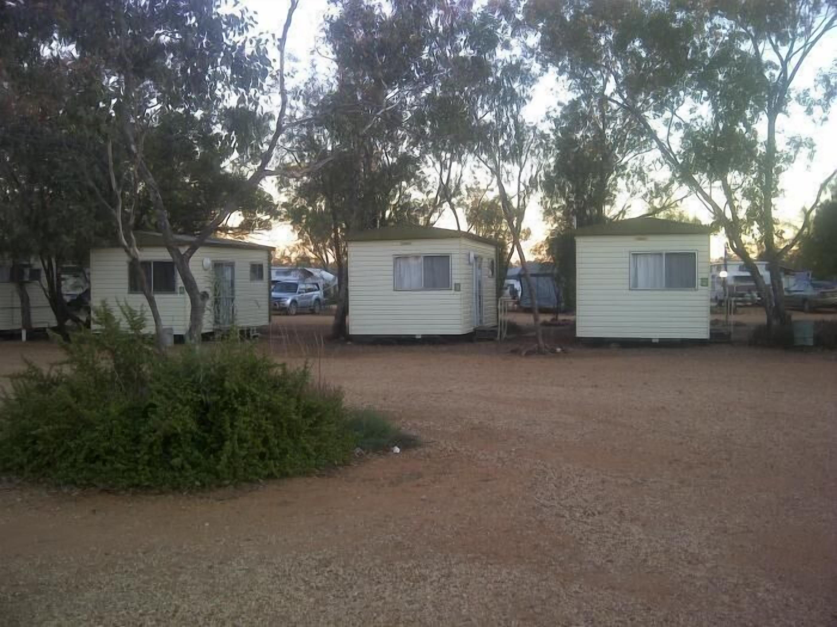 Um camping com várias casas móveis pequenas e térreas, cercado por árvores e chão de cascalho.
