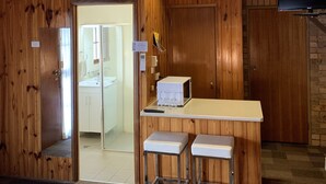 A wooden interior with a kitchenette, a TV mounted on the wall, and a door leading to a bathroom.