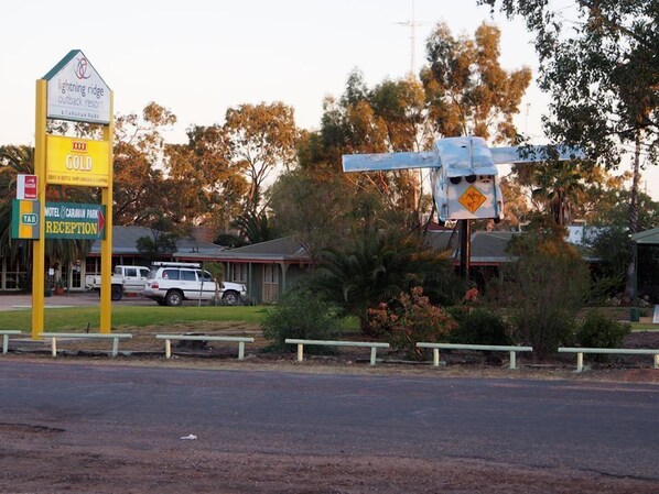 A motel sign with a reception area, a gold sign, and a car parked in front.