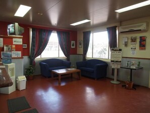 A waiting area with two blue armchairs, a wooden table, a water dispenser, and a bulletin board with notices.