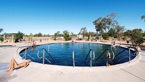 A swimming pool with a clear blue sky, surrounded by trees and a few structures.