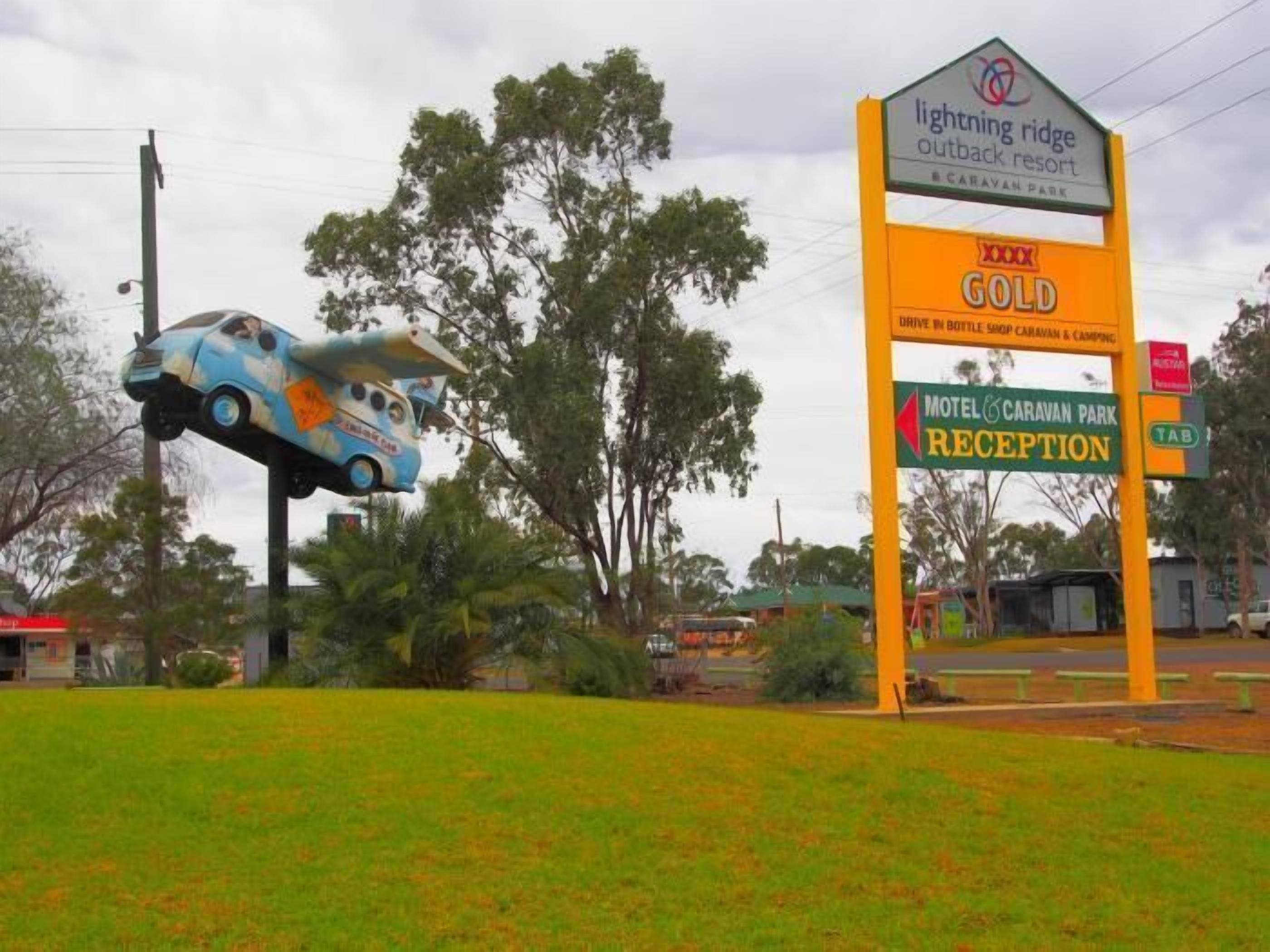 A sign for Lightning Ridge Outback Resort with a gold award, a reception area, and a car sculpture.
