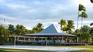 Una cancha de voleibol de playa con una pérgola, palmeras y un cielo despejado.