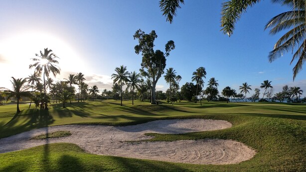 Un campo de golf con búnkeres de arena, palmeras y un cielo despejado.