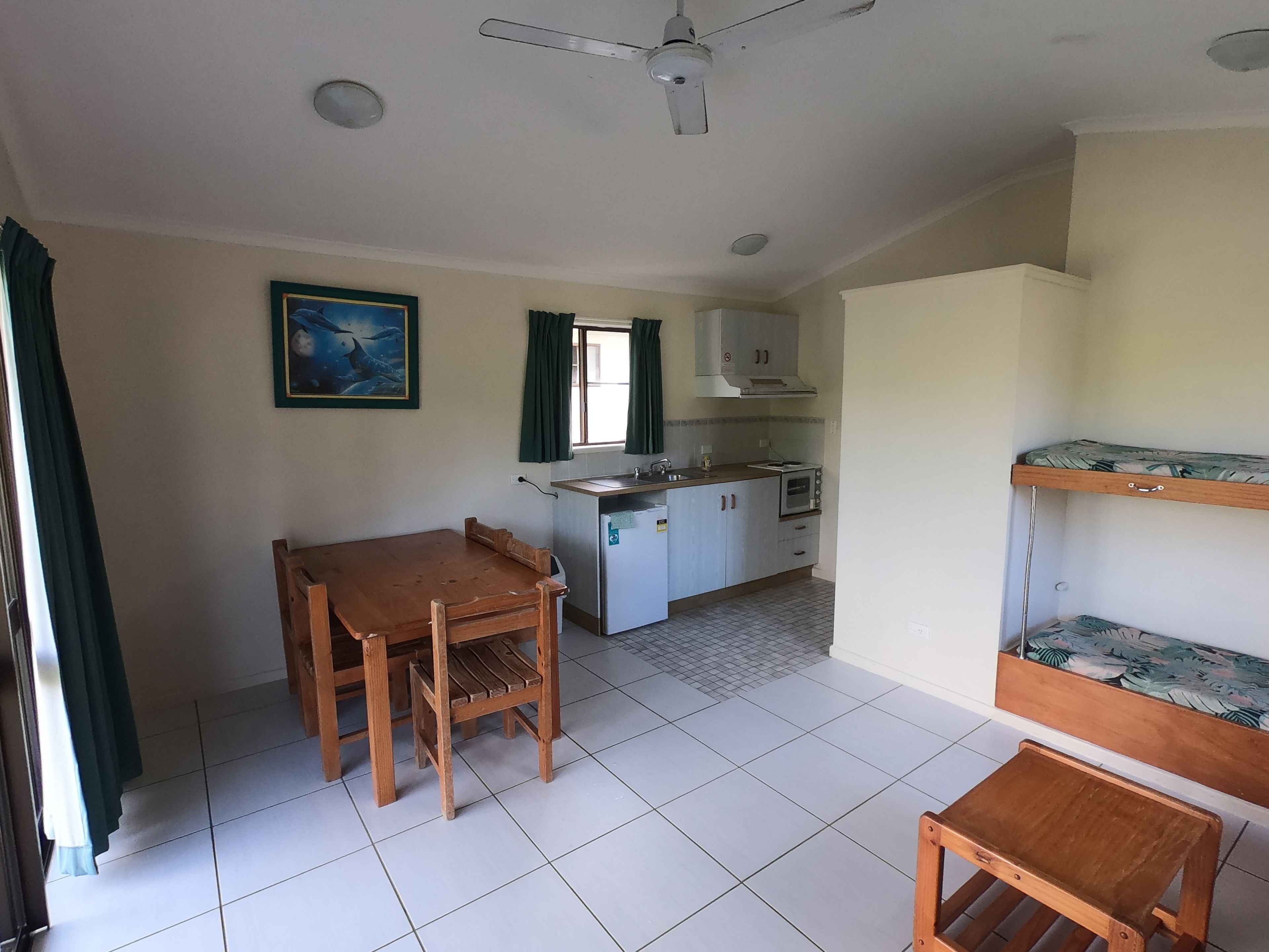 Una cocina compacta con una mesa de comedor, sillas, horno empotrado y un refrigerador pequeño.