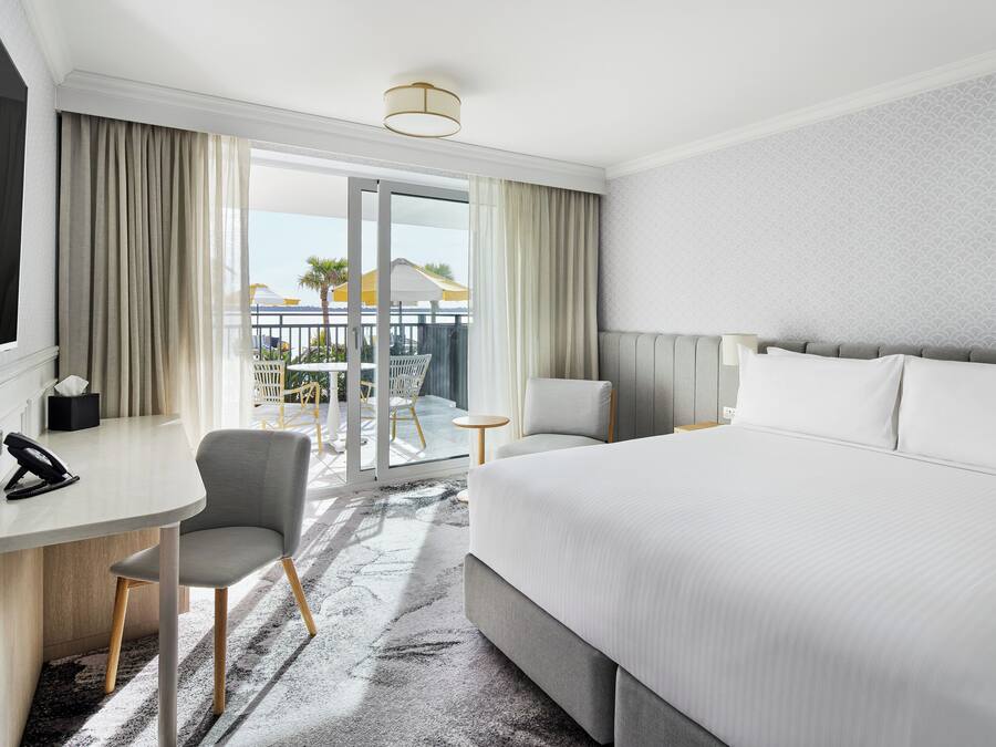 A hotel room with a bed, a desk, a chair, a phone, and a view of the outside.