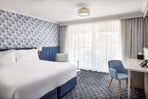 Habitación de hotel con una cama grande, un escritorio, una silla, una mesita y una ventana con cortinas.