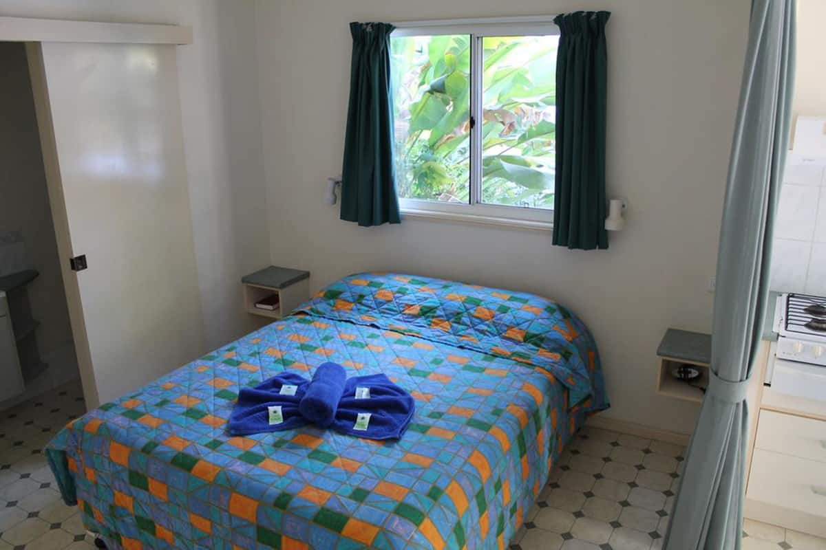 Ein Schlafzimmer mit Bett, einem Fenster mit Vorhängen, einer kleinen Ablage und einem Heizkörper.