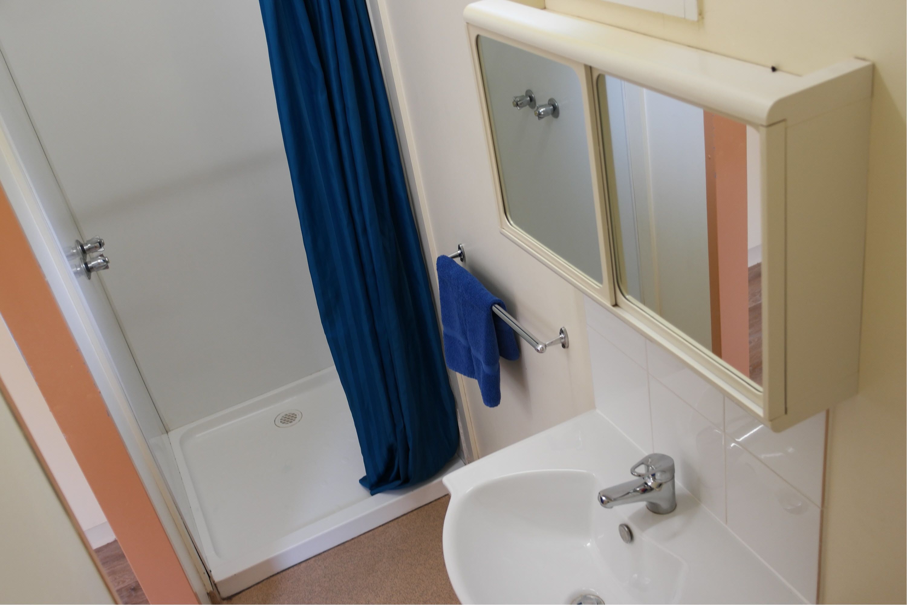 A bathroom with a shower, a sink, a mirror, and a towel rack.