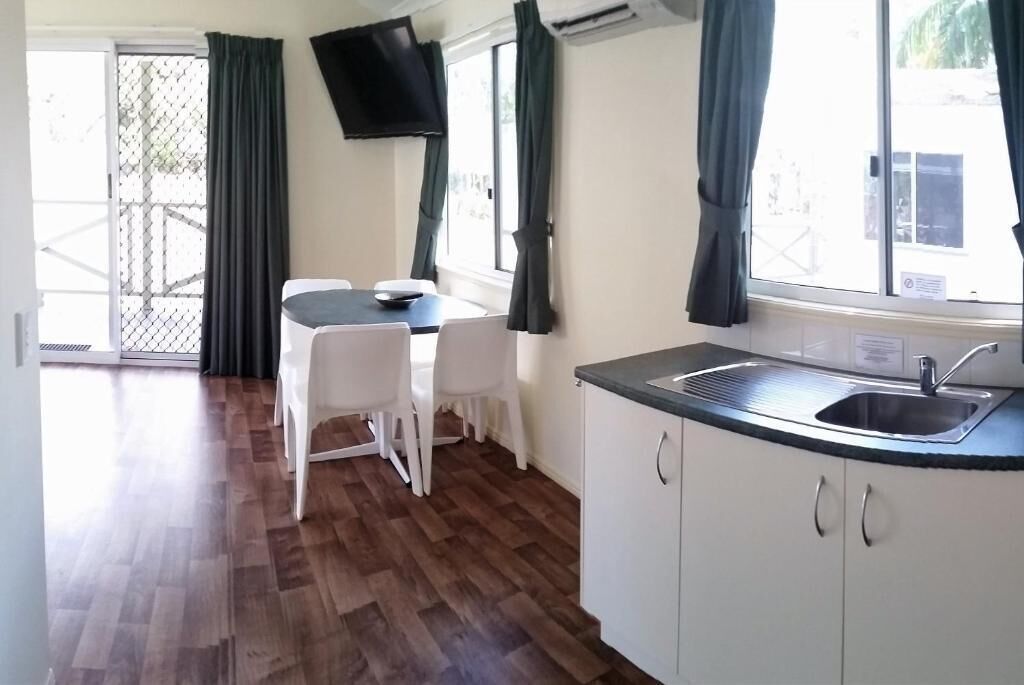 A compact kitchen with a sink, white cabinets, and a dining table with chairs.