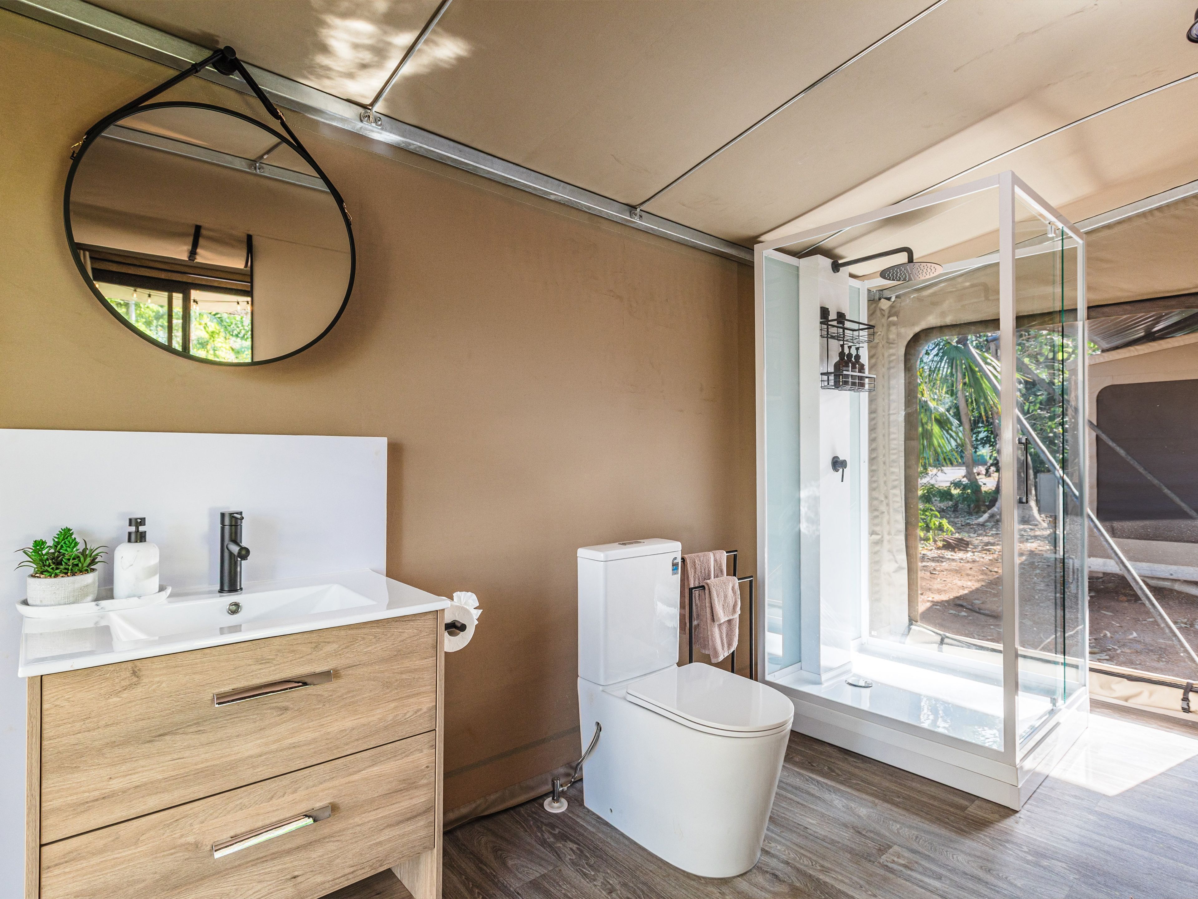 A modern bathroom with a wooden vanity, a toilet, and a glass-enclosed shower.