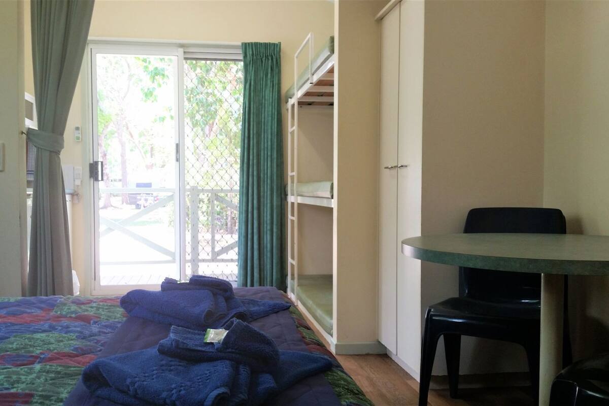 Ein Zimmer mit einem Bett, einem Schreibtisch und einem Stuhl. Eine Glastür führt in einen Außenbereich.