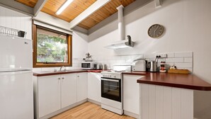 Cozinha moderna com armários brancos, bancada de madeira, forno embutido, micro-ondas e janela com vista para o verde.