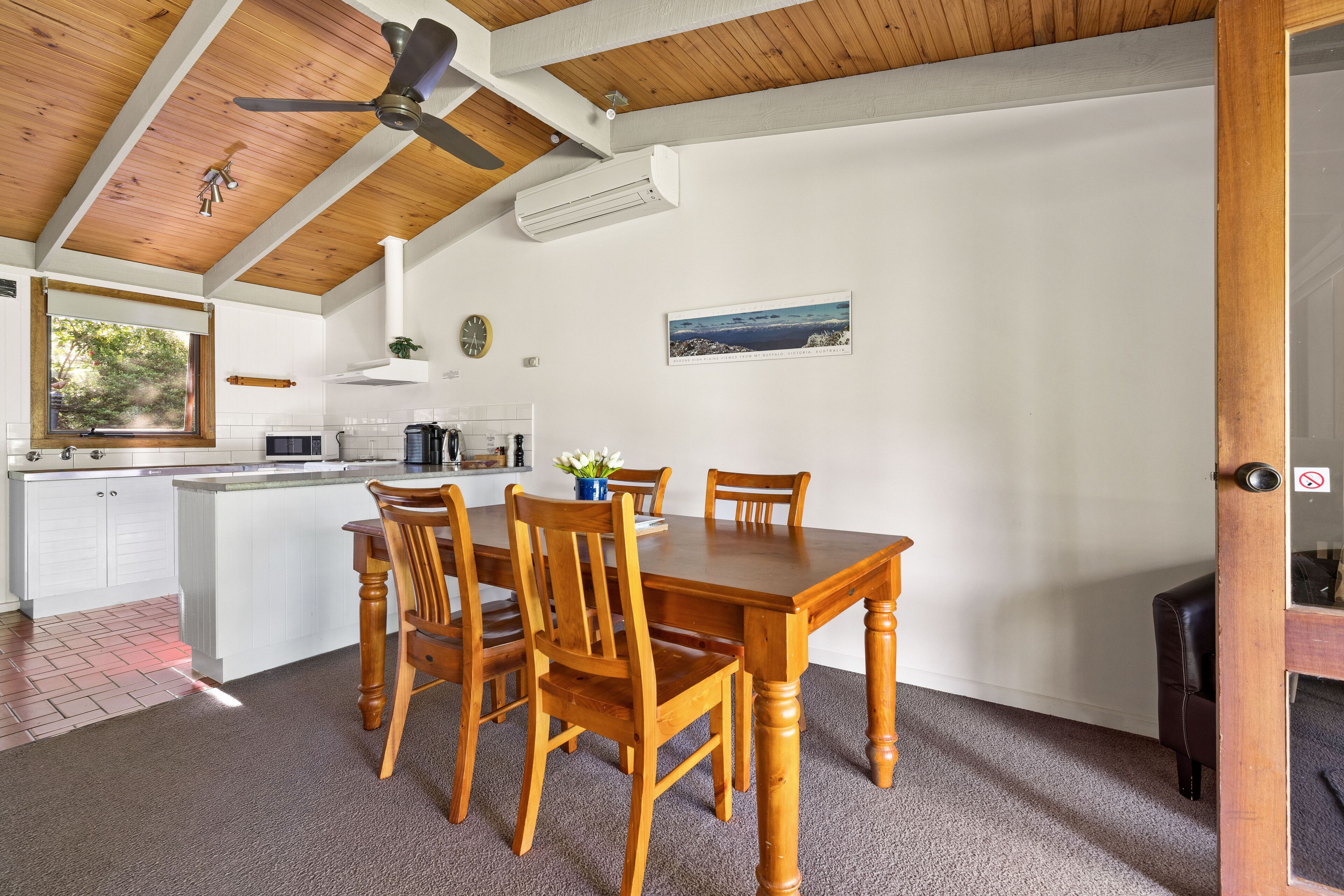 Een eetgedeelte met een houten tafel en stoelen, een plafondventilator en uitzicht op de keuken.