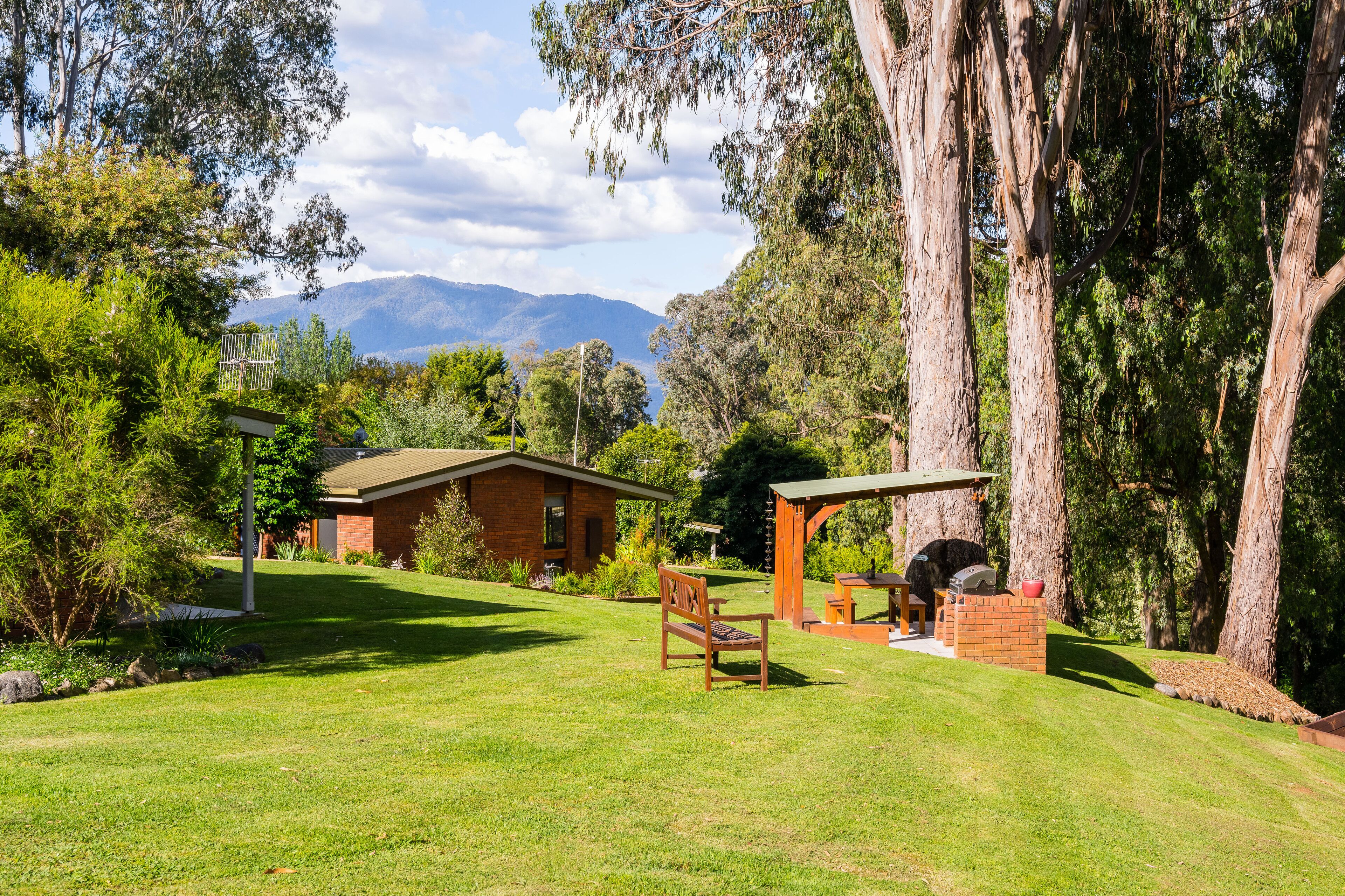 A well-maintained backyard with a barbecue area, a wooden bench, and a brick structure.