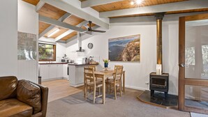 Uma cozinha moderna com vigas de madeira, sala de jantar com mesa e cadeiras, sofá de couro marrom e lareira a lenha.