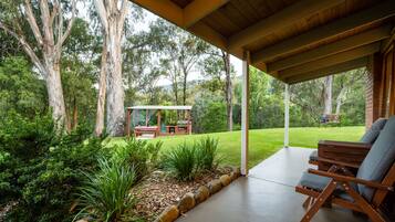 Relax in a serene outdoor space surrounded by lush greenery and shaded by a wooden roof structure.
