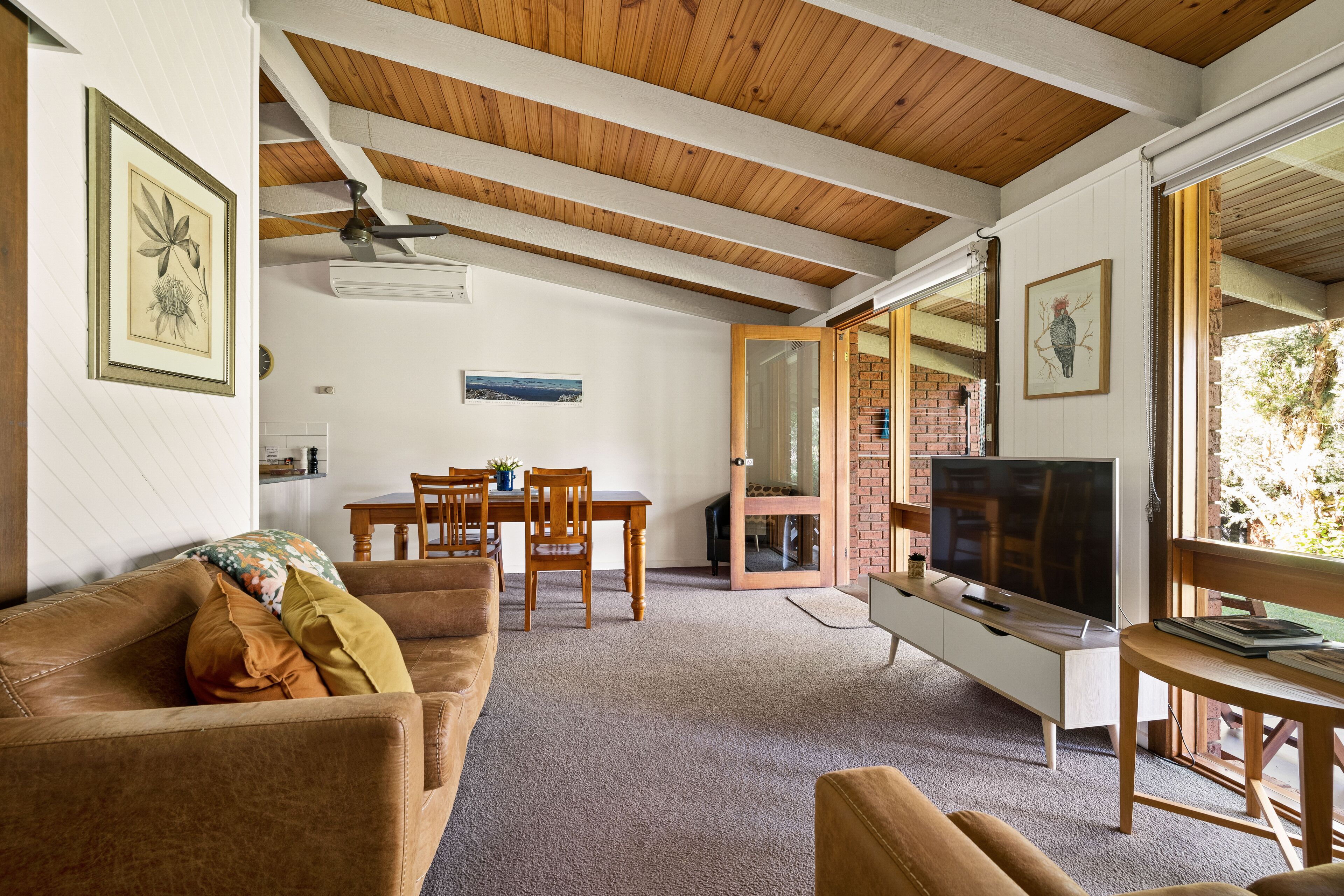 A living room with a wooden ceiling, a TV, a sofa, and a dining area.
