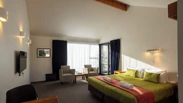 A hotel room with a large bed, two armchairs, a desk, and a television.