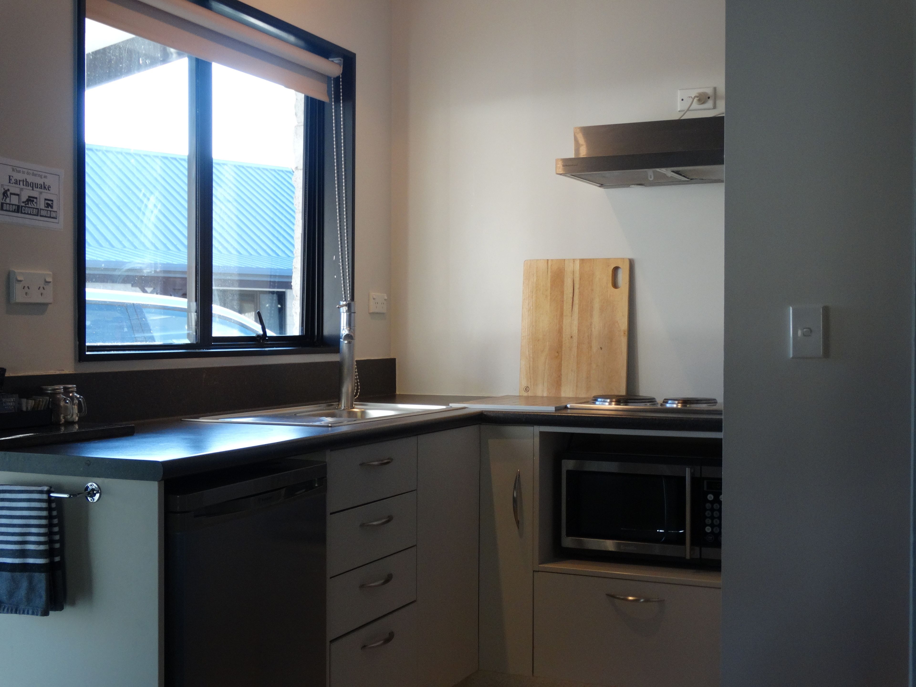 A compact kitchen with a window, a microwave, a wooden cutting board, and a dishwasher.