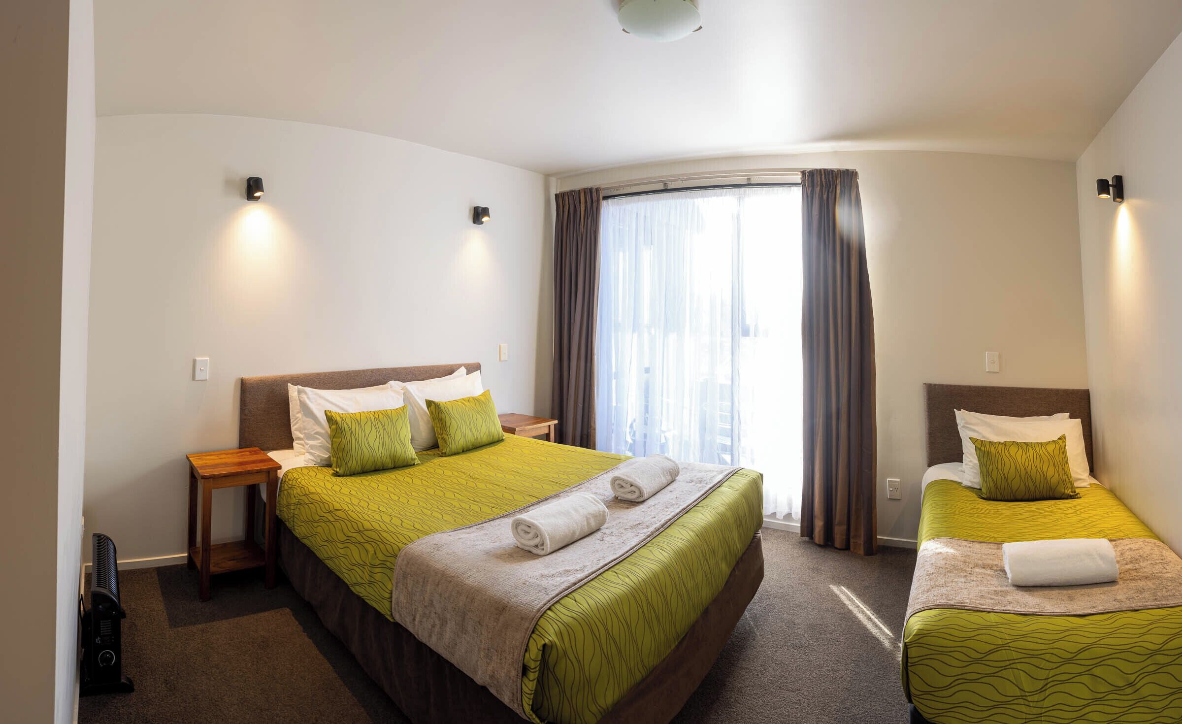 Una habitación de hotel con una cama grande, una cama más pequeña, una mesita de noche y un calefactor.