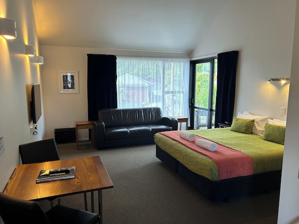 Habitación de hotel con cama, sofá, mesa con un control remoto y televisor montado en la pared.