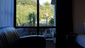 A room with a large window offering a view of a mountainous landscape and a palm tree. - Alpine Glacier Motel (Franz Josef Glacier)