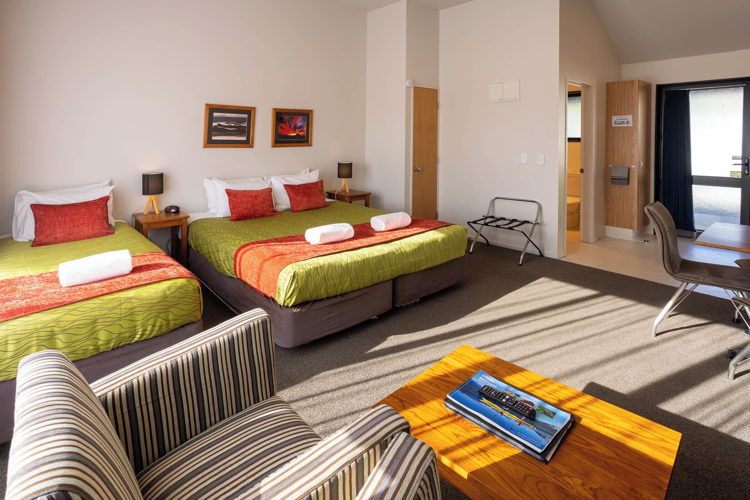 Habitación de hotel con dos camas, un sofá, una mesita con una revista y vistas al exterior.