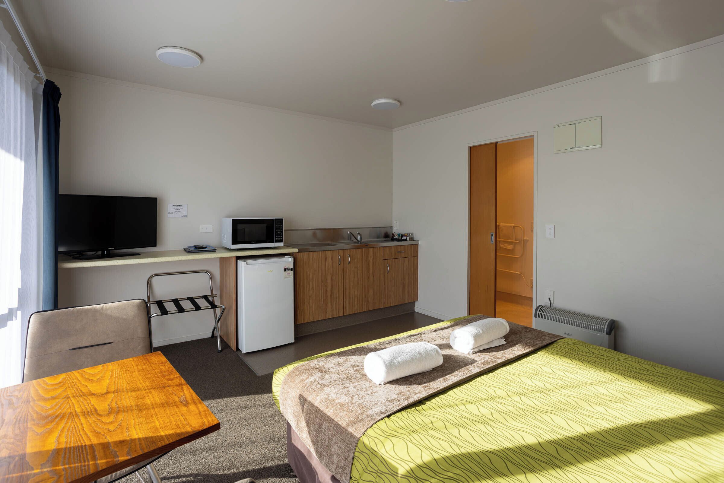 Een hotelkamer met een bed, een bureau met een computer, een kleine kitchenette en een televisie.