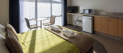 A hotel room with a bed, a desk, a television, a microwave, and a small refrigerator.