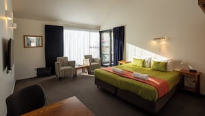 A hotel room with a large bed, a desk, two chairs, a TV, and a window with curtains. - Alpine Glacier Motel (Franz Josef Glacier)