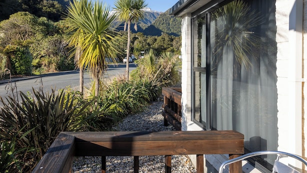 A wooden bench outside a building with a view of a road and mountains. - Alpine Glacier Motel (Franz Josef Glacier)