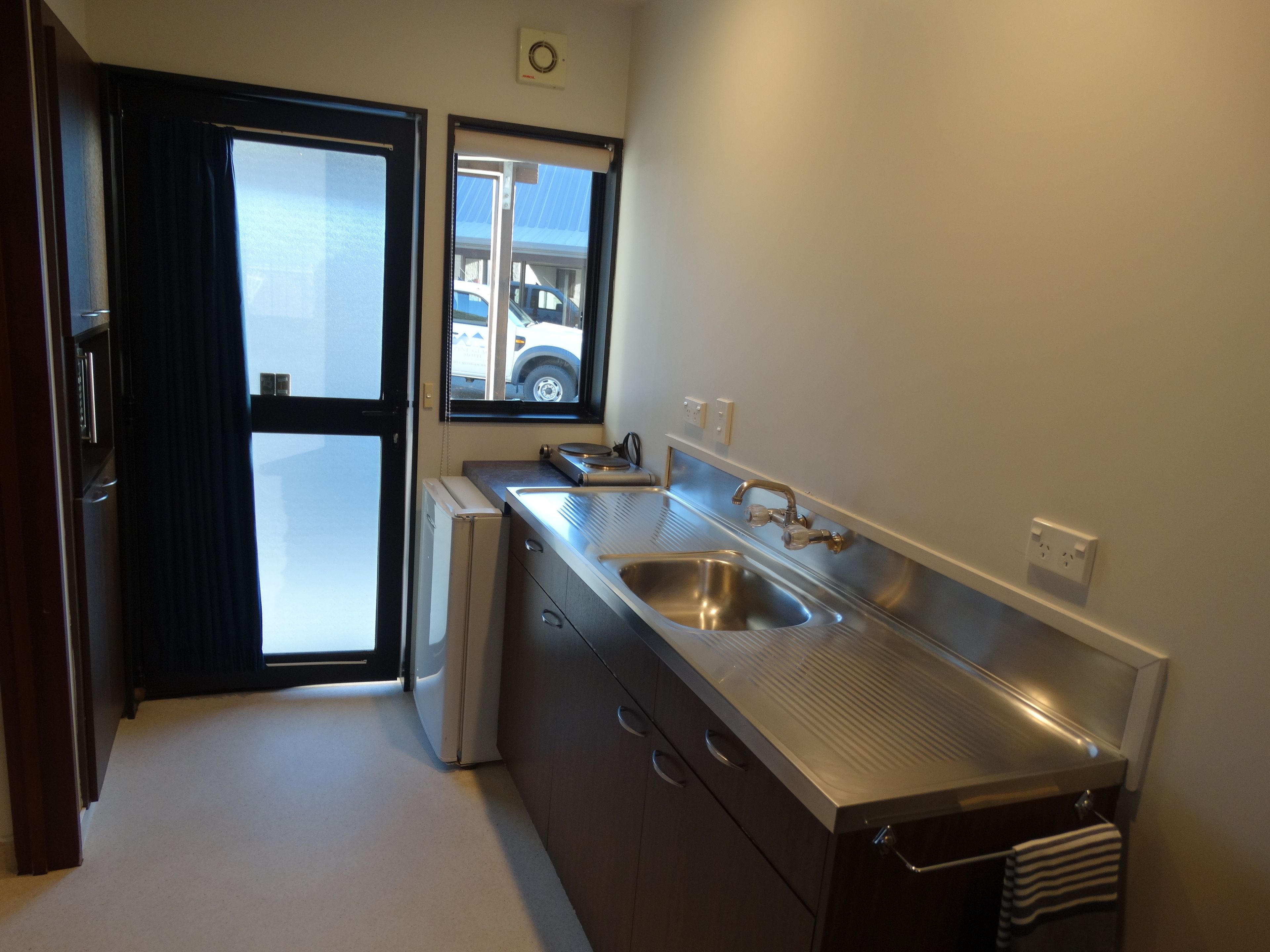 A modern kitchen with stainless steel appliances, a large sink, and a window overlooking a parking area.