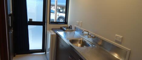 A modern kitchen with stainless steel appliances, a large sink, and a window overlooking a parking area.