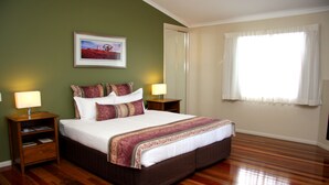 A large bed with a brown headboard, two bedside tables, a nightstand, and a framed picture on the wall. - Yabbaloumba Retreat (Cambroon)