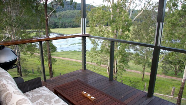 A wooden deck with a sofa and table, overlooking a river and greenery. - Yabbaloumba Retreat (Cambroon)