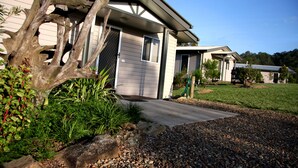 A residential house with a gravel driveway, a wooden tree in the front yard, and a clear blue sky. - Yabbaloumba Retreat (Cambroon)