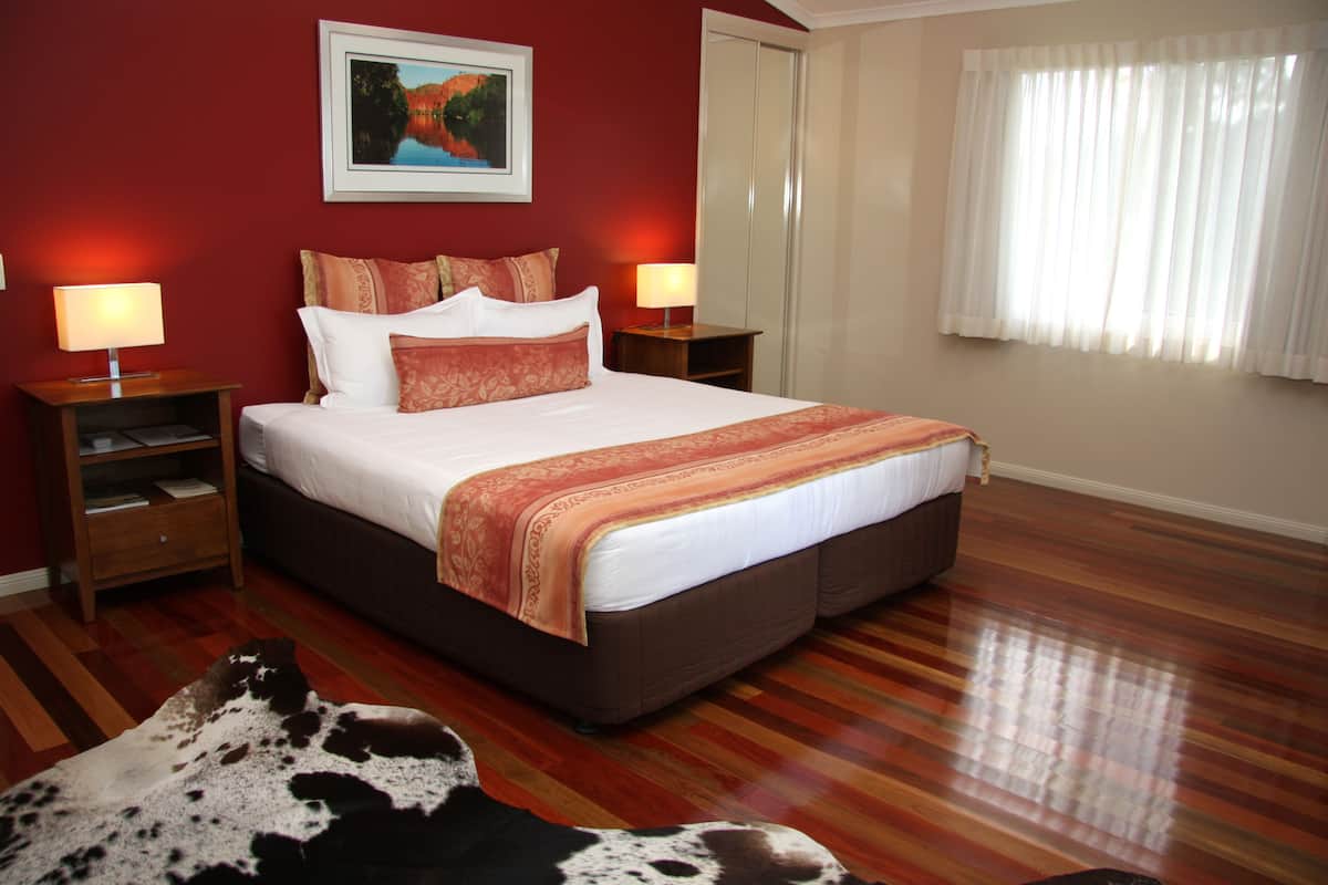 A bedroom with a large bed, two bedside tables with lamps, a wooden floor, and a cowhide rug.