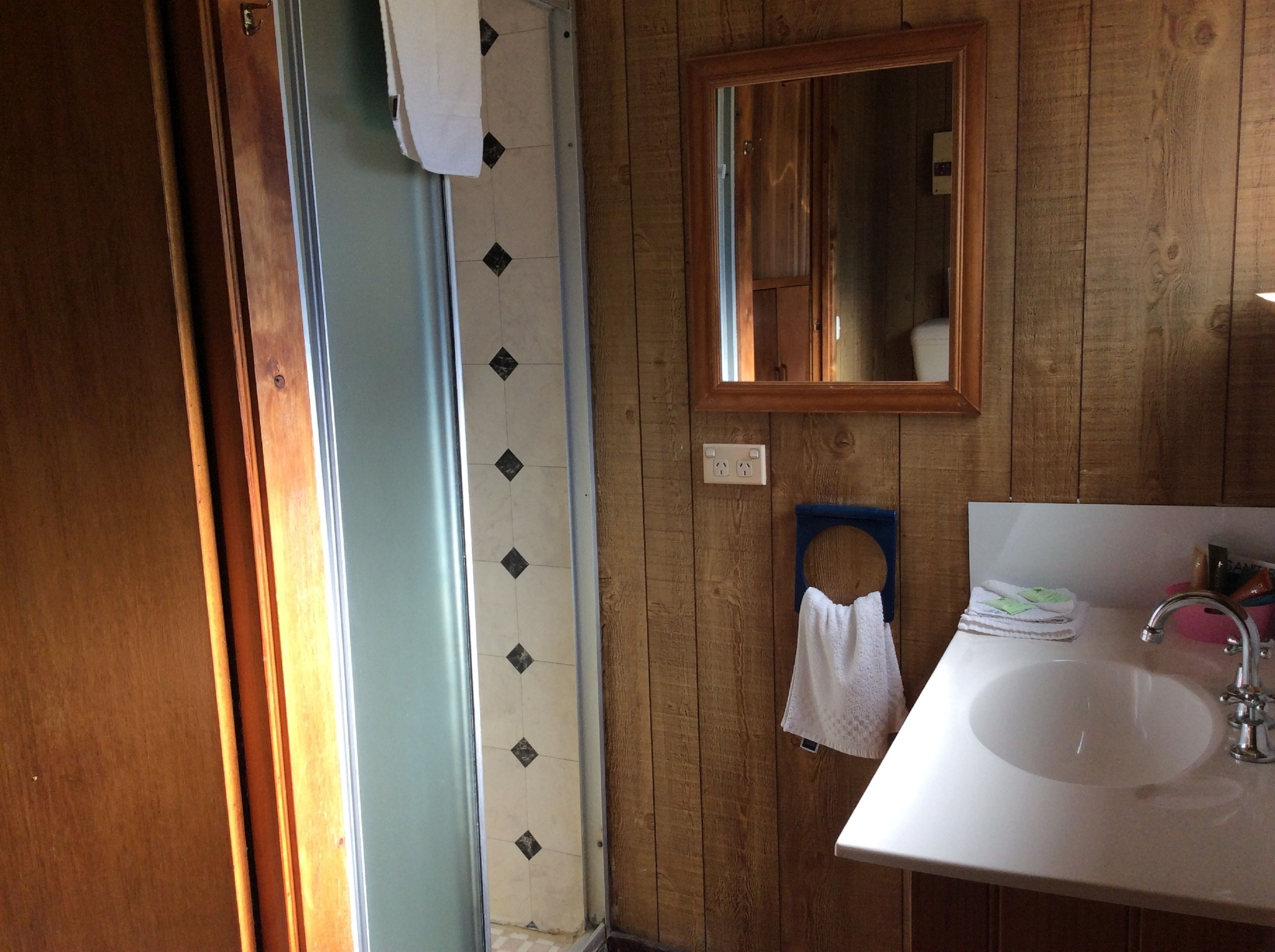 Un baño con pared de madera, un lavabo blanco, un espejo y un perchero para toallas.