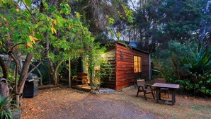 Un chalet rustique en bois, doté d’une véranda et entouré d’une végétation luxuriante et d’arbres.