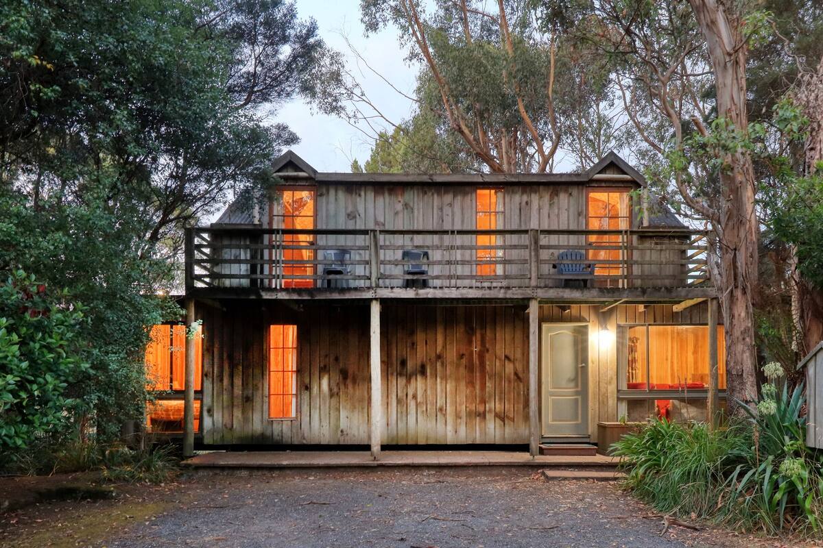 Un chalet rustique en bois doté d’un balcon, entouré d’une forêt dense.